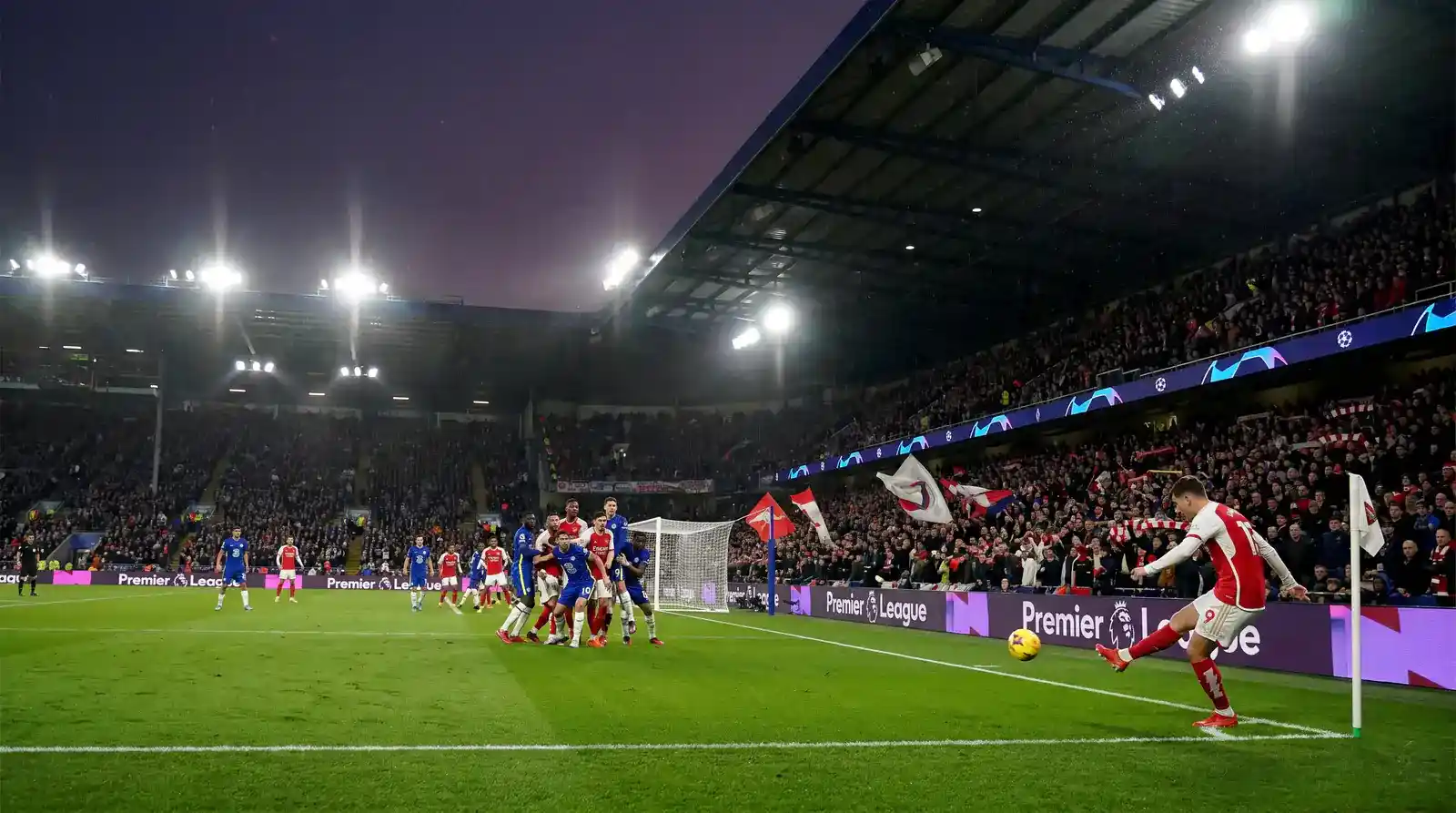 Premier League corner kick being taken with the attacking side crowding the six-yard box at a packed stadium