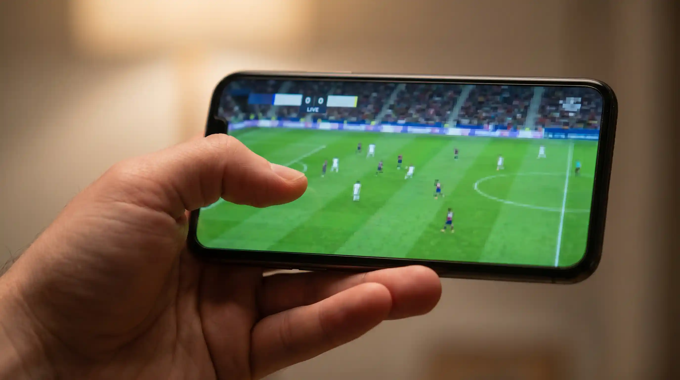 Hand holding a smartphone showing the closing minutes of a live football match with a live score graphic at the top of the screen